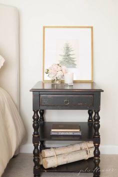 a nightstand with books and a candle on it next to a bed in a bedroom