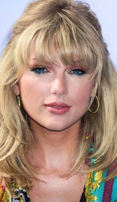 a close up of a person with long blonde hair and blue eyeshadow wearing earrings