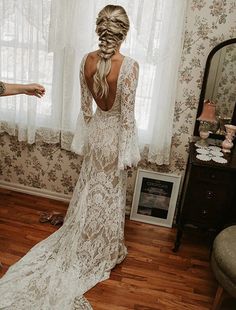 a woman standing in front of a window wearing a white wedding dress with long sleeves