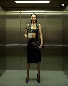 a woman standing in front of an elevator holding a potted plant with her hands on her hips