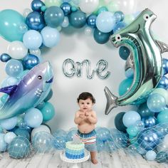 a little boy standing in front of a cake surrounded by blue and silver balloon decorations