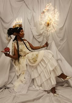 a woman sitting on top of a white sheet covered floor next to a vase with flowers