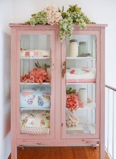 an old china cabinet painted pink with flowers on the top and glass doors that are open