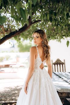 a woman standing under a tree wearing a wedding dress with an open back and floral appliques