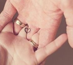 two people holding hands with rings in the shape of a heart on their fingers,