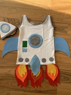 a child's space shuttle shirt made out of construction paper and felt, on a wooden floor