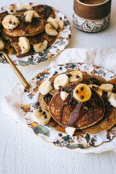 two plates filled with pancakes covered in banana slices and chocolate syrup next to a cup of coffee