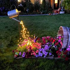 a garden with flowers and lights in the grass next to a wooden barrel filled with water