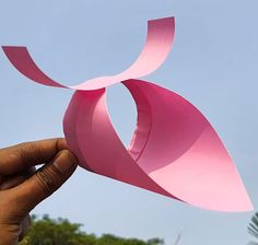 a hand holding up a pink piece of paper that looks like an origami