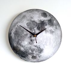 a clock made to look like the moon is shown on a white wall with black hands