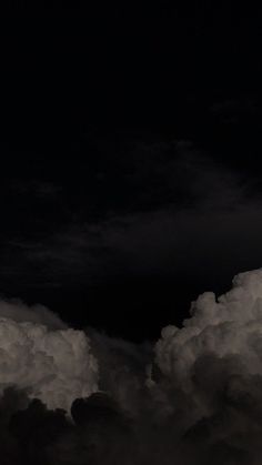 an airplane is flying high in the sky with dark clouds behind it at night time