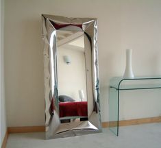 a mirror sitting on top of a white floor next to a glass table and vase