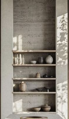 a shelf with bowls and vases on it in front of a wall filled with shelves