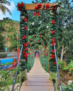 a wooden walkway covered in vines and red flowers next to a forest filled with palm trees