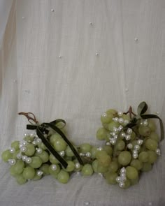 two bunches of grapes with pearls on them sitting on a white cloth covered table