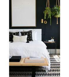 a bedroom with black walls, white bedding and plants hanging above the headboard