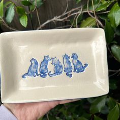 a hand holding a blue and white ceramic plate with cats on it's side