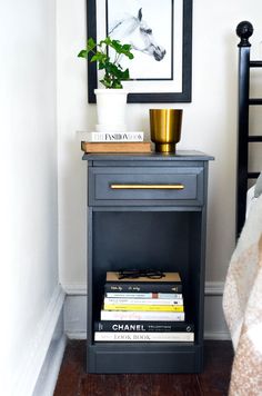 a nightstand with books and a potted plant on it next to a framed photograph