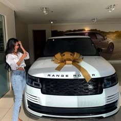 a woman standing next to a range rover with a bow on it