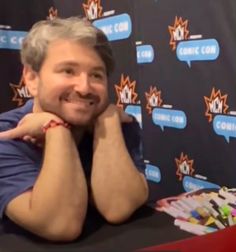 a man sitting at a table with his hands on his chin and smiling for the camera