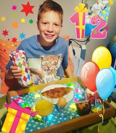 a young boy sitting in front of a birthday cake with balloons and confetti