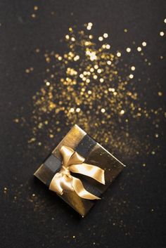 a gift box with a gold bow on it and some confetti sprinkles in the background