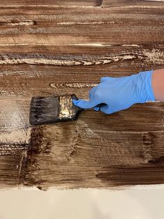 a person in blue gloves is holding a paintbrush and painting on wooden planks