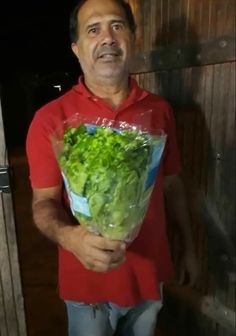 a man holding a bag of lettuce in front of a wooden door at night