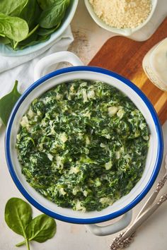 a bowl filled with spinach on top of a wooden cutting board next to other foods