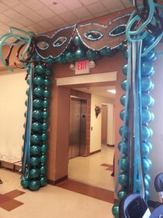 an arch decorated with blue and green balloons for a party or event in the hallway