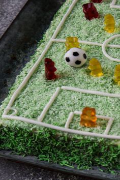 a cake shaped like a soccer field with gummy bears around it and a soccer ball on top