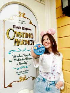 a woman is holding up a sign in front of a yellow building that says castle kingdom casting agent