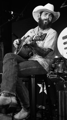 a man sitting on top of a stool with a guitar in his hand and wearing a cowboy hat