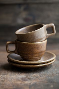 two cups and saucers sitting on top of a wooden table next to each other