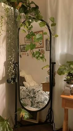 a mirror sitting on top of a wooden table next to a plant filled wall in a room