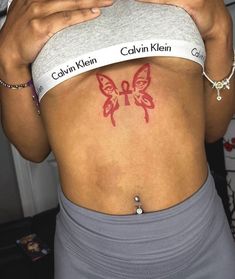 a woman with a red butterfly tattoo on her stomach is holding a cell phone up to her chest