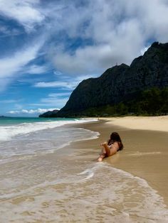 a woman laying on top of a sandy beach next to the ocean with mountains in the background