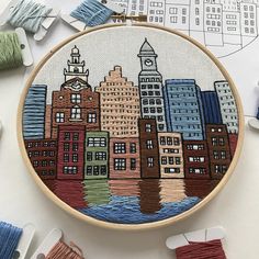 an embroidery project with buildings on it and some thread spools next to it