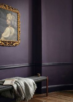 a bench in front of a purple wall with a gold framed painting on the wall