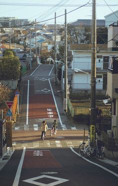 two people walking down an empty street in the middle of town with houses on either side