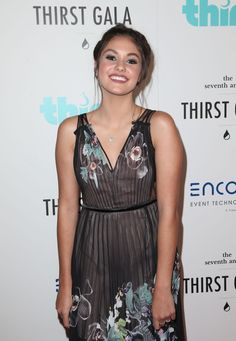 a woman in a black dress smiles for the camera on a red carpet at an event