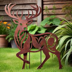 a metal deer sculpture sitting on top of a green grass covered field next to flowers