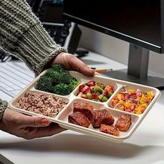 a person holding a tray full of food in front of a computer screen on a desk