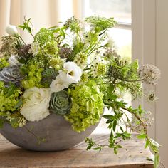 a vase filled with lots of flowers on top of a wooden table next to a window