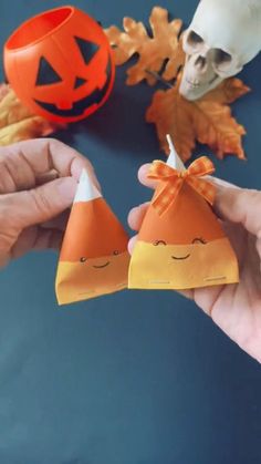 two hands holding small cones with faces on them, one has a pumpkin and the other has a jack - o'- lantern