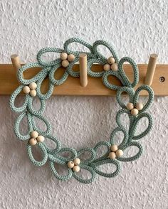 a green and white crocheted wreath hanging on a wooden coat rack with pegs