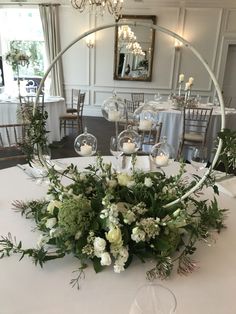 an arrangement of flowers and greenery on a table in a room with chandeliers