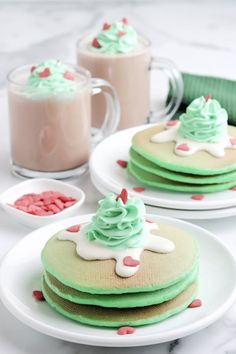 two plates with green and white desserts on them next to cups of hot chocolate