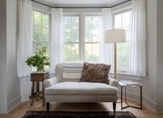 a white couch sitting under a window next to a table with a lamp on it