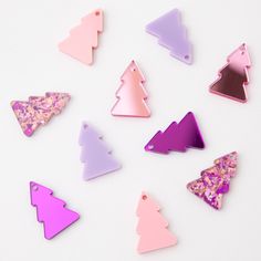 several different colored christmas trees on a white surface with glitter in the bottom and pink, purple, and green shapes